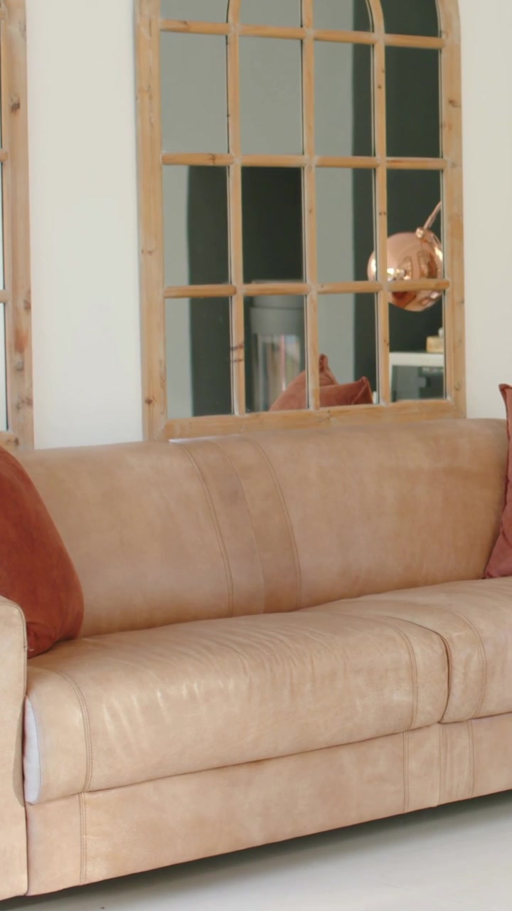 Vertikal video: Panorerende kamera viser beige sofa med rustfarvede puder og kobberlampe i stuen.