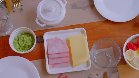 table top view with breakfast served, it can be seen that there is coffee, fruits, ham, cheese and homemade bread