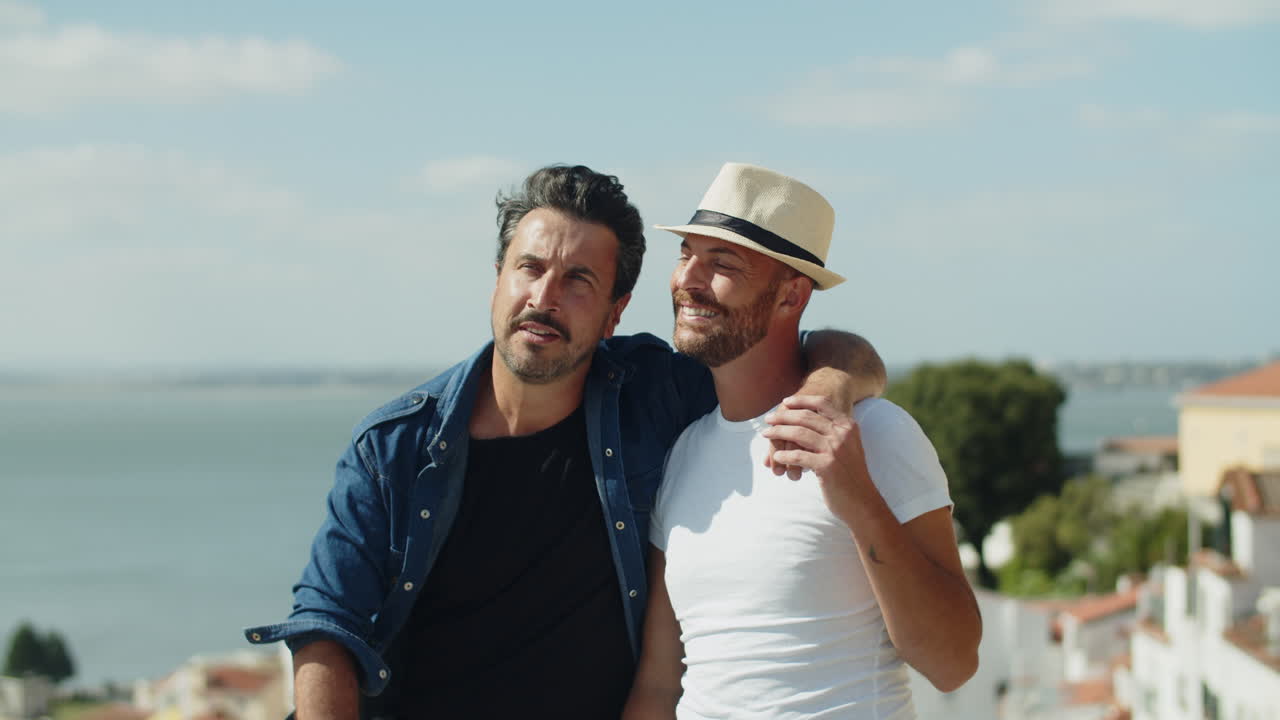 Happy homosexual man sitting and hugging lover's shoulder with incredible views