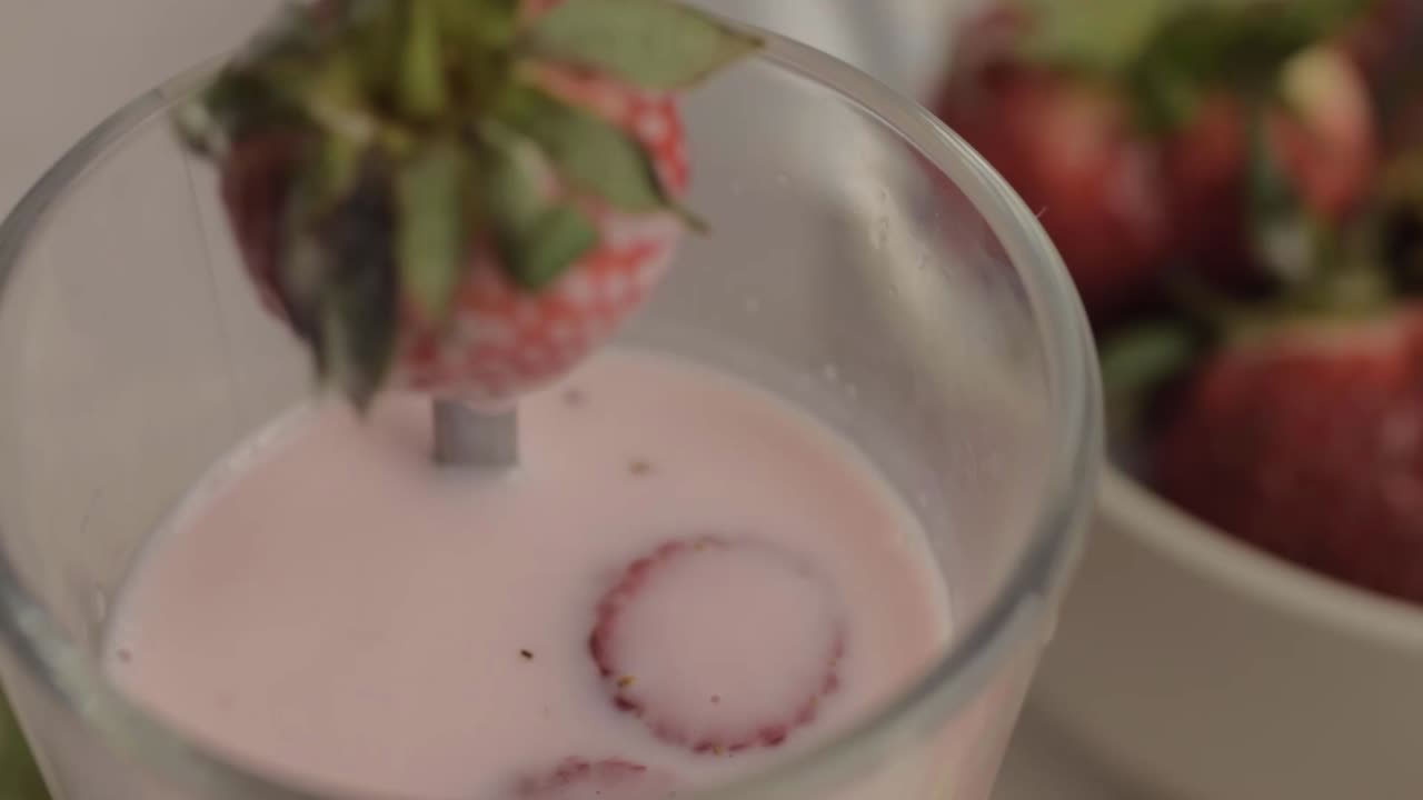 Primer plano de una mano preparando un batido de fresa con fruta fresca