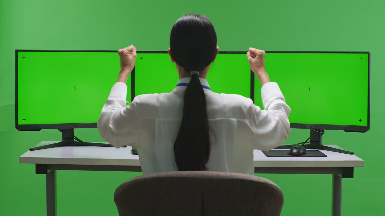 트리플 모니터 녹색 화면 앞에서 성공을 축하하는 여성