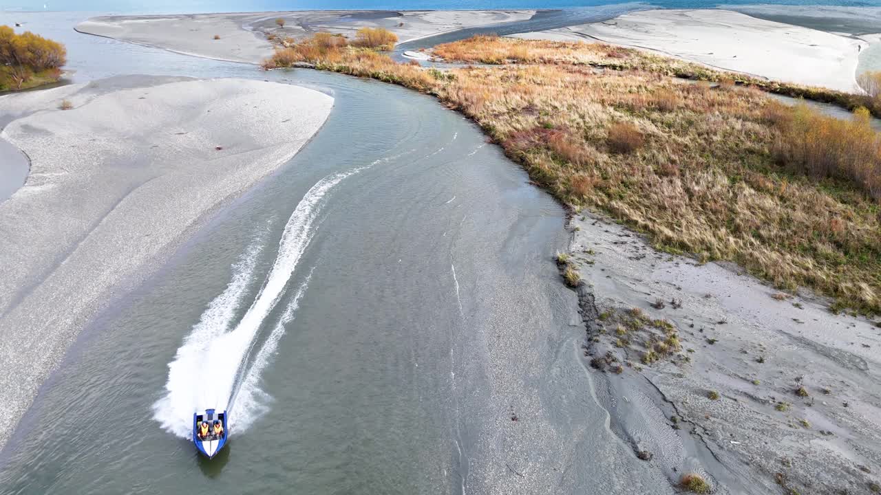 A speedboat swiftly maneuvers through a winding river in Glenorchy, New Zealand, surrounded by rugged landscapes and vibrant foliage