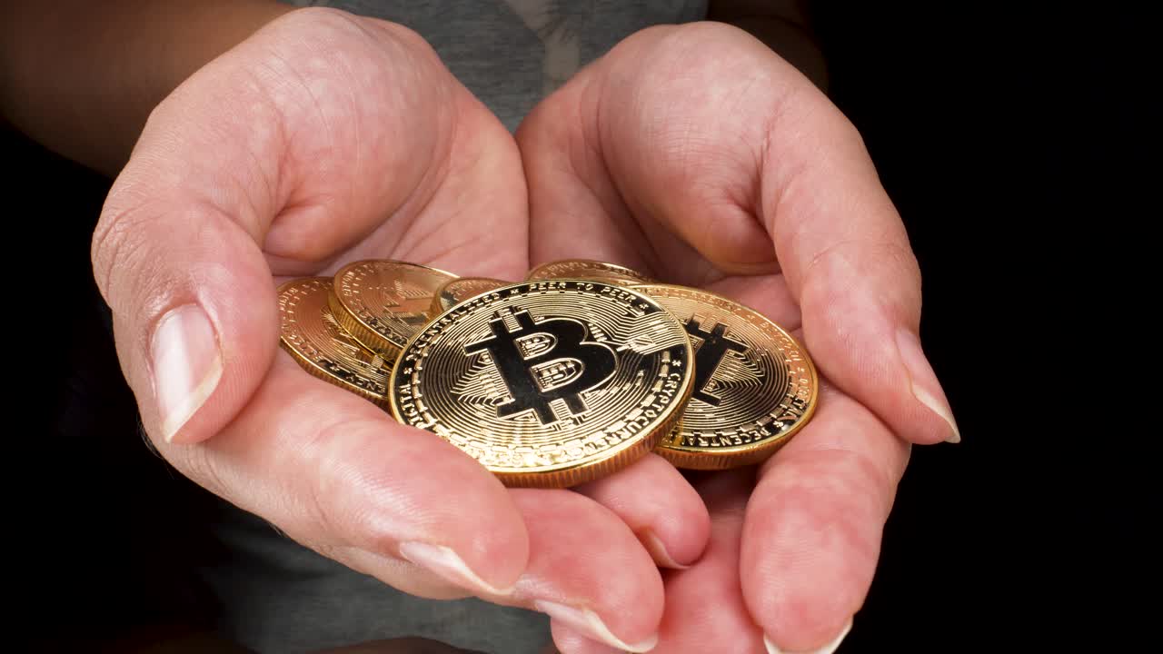 manos femeninas jóvenes sosteniendo bitcoins dorados en vista macro de fondo negro aislado 4k, inversión en criptomonedas