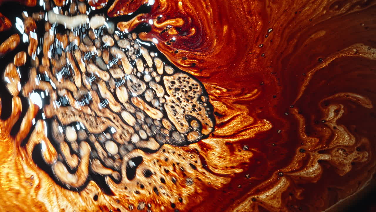 Swirling brown and gold liquid creating abstract patterns, captured in a macro close-up shot