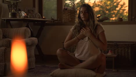 young female latin meditating sitting on a pillow in casual indoor spiritual studio with big green window with vegetation in a wooden home slow motion 60 fps
