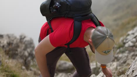 caucasian male hiker in red shirt with backpack climbs up steep rocky slope