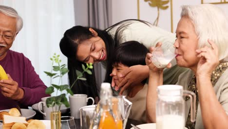three generations enjoy breakfast together at a bright dining table, sharing food, laughter, and affectionate moments in a warmly lit home environment
