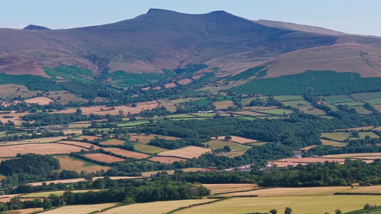 La cima del monte Pen y Fan che si erge sopra terreni agricoli aridi nel Parco Nazionale Brecon Beacons, Galles, con campi agricoli estivi inariditi in primo piano