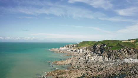 aerial shot of a rocky coastline with a lighthouse in the distance