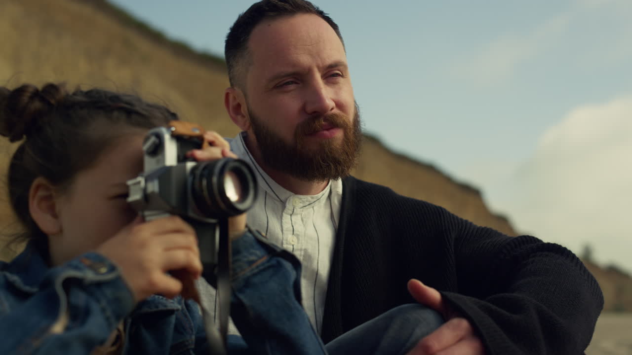 해변에서 사진을 찍는 초점을 맞춘 소녀. 자연 풍경을 즐기는 가족.