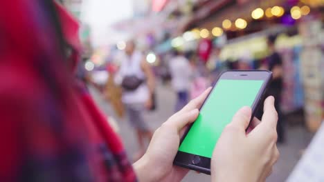 una mujer asiática con mochila sonriendo y usando un teléfono inteligente de pantalla verde viajando sola vacaciones al aire libre en la calle de la ciudad en khao san road en bangkok bangkok - tailandia.