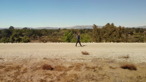 Swooping-drone-and-portrait-shot-of-man-walking-along-path-on-ridge-overlooking-forrest-and-mountains