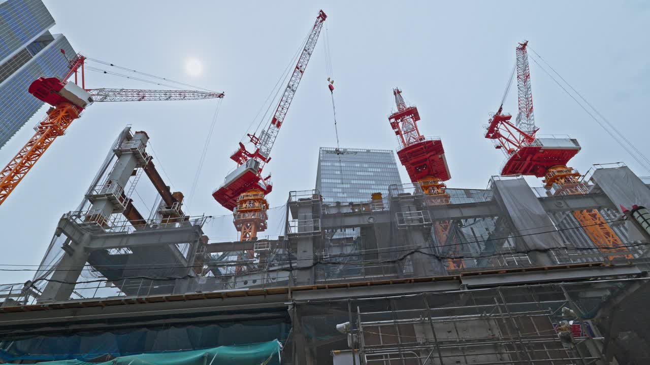 A dynamic shot of multiple construction cranes towering over Tokyo, actively engaged in building the city's future landscape.