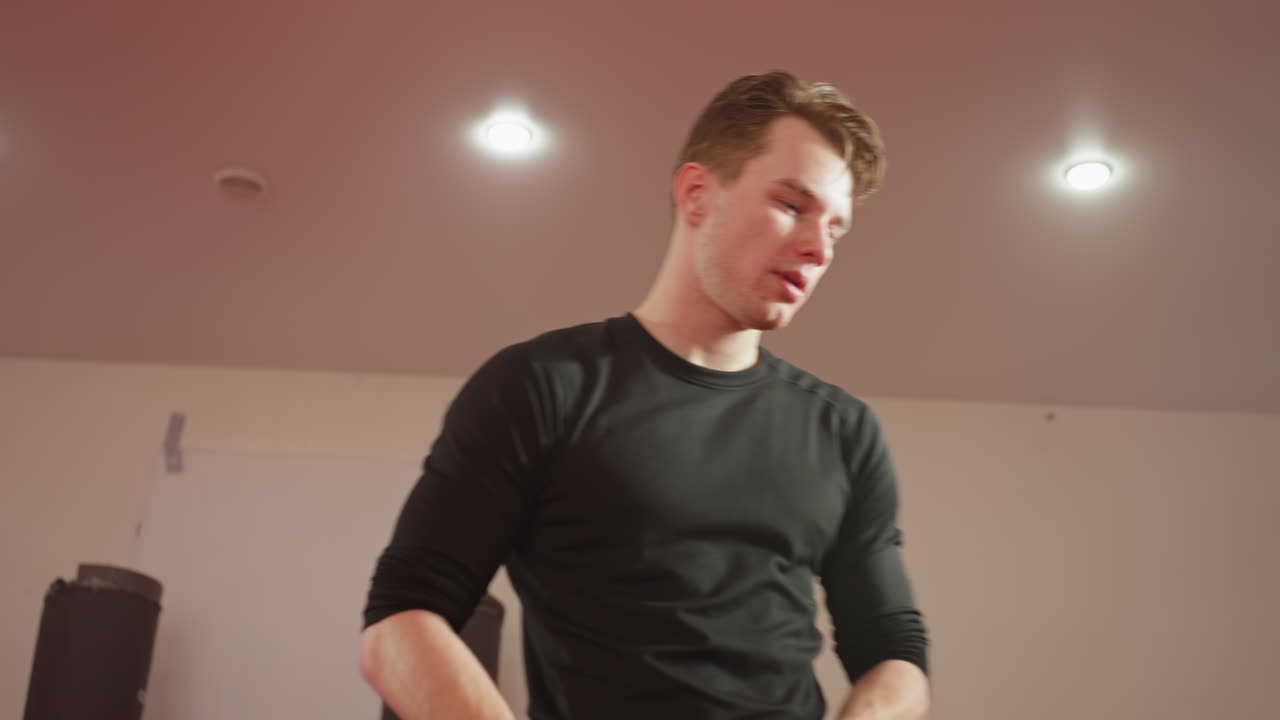 Boxer adjusting gloves after training session in gym under bright lights, wearing black shirt, focused expression, preparing for next workout, showing discipline, strength, determination in combat sports