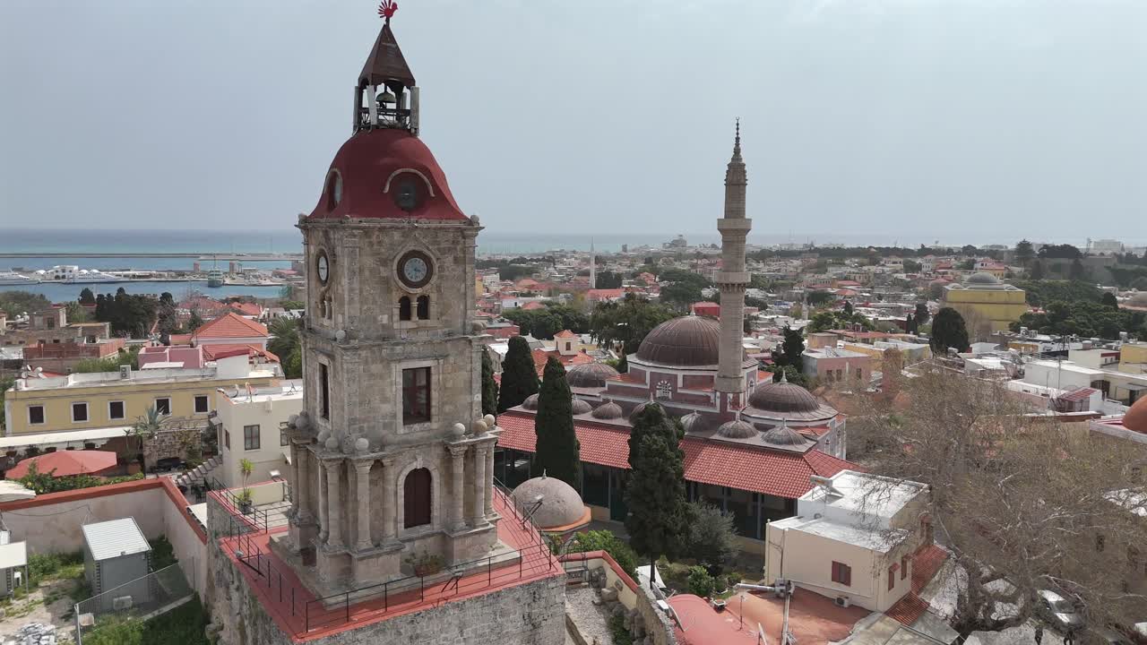 Aerial view backwards from the Medieval Clock Tower (Roloi Clock Tower) and The Suleyman Mosque in the city of Rhodes in Rhodes island in Greece.Harbor and old town at the background on a sunny day.