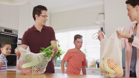 feliz familia caucásica desempaquetando bolsas con verduras