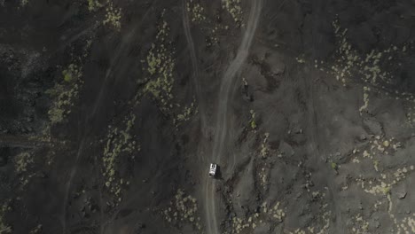 Jeep-driving-through-black-volcanic-sand-field-in-Bali,-top-down