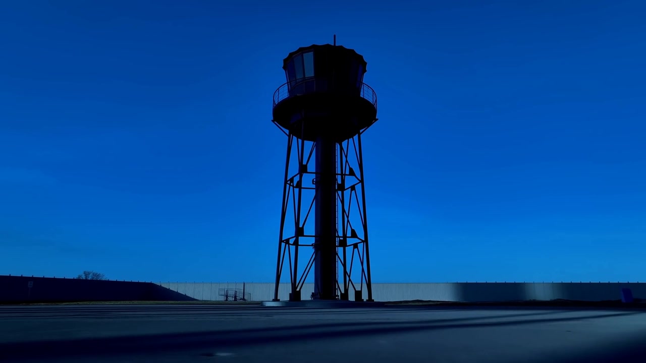 Shifting sunlight casting long shadows across open paved area, revealing elevated metal tower cabin