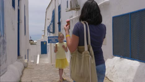 young mother doing photo to daughter on narrow street background in summer city