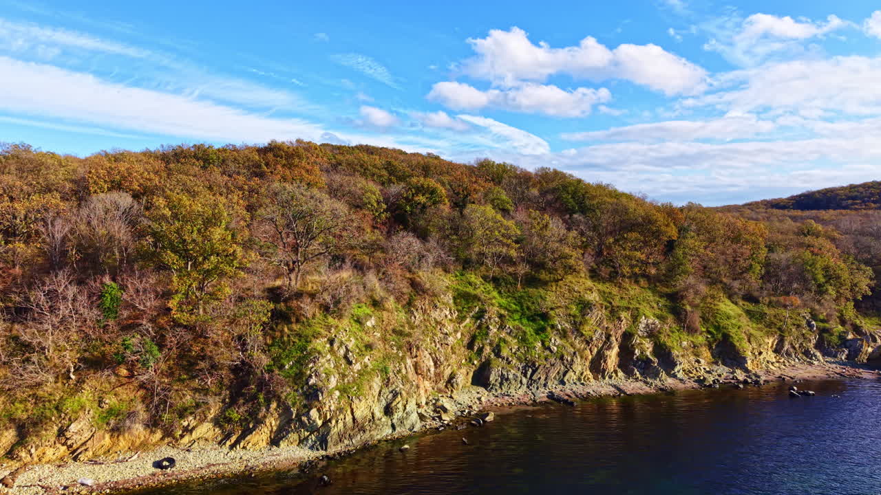 Naturskøn kystlinje med farverigt efterårsløv under en klar, blå himmel ved middagstid
