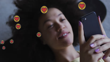 animation of hearts over happy african american woman using smartphone