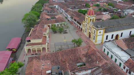 the drone glides smoothly over the red colonial rooftops of mompox, rolling right while yawing left to create a sweeping, cinematic motion. the majestic church of maría inmaculada comes into view.