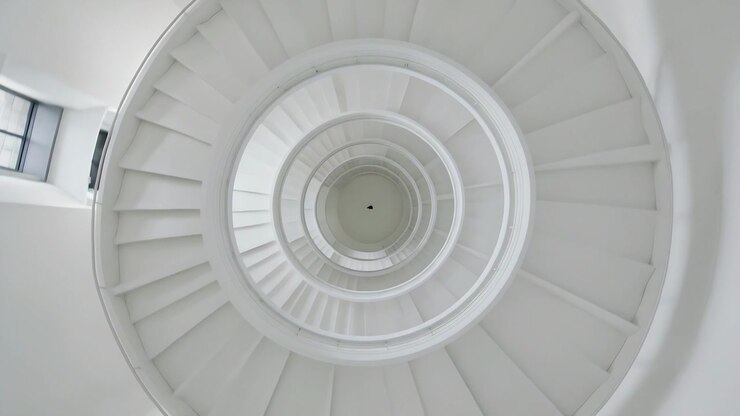 Cámara giratoria encuadrando una escalera de caracol blanca dentro de una rotonda, resaltando un elemento oscuro central.