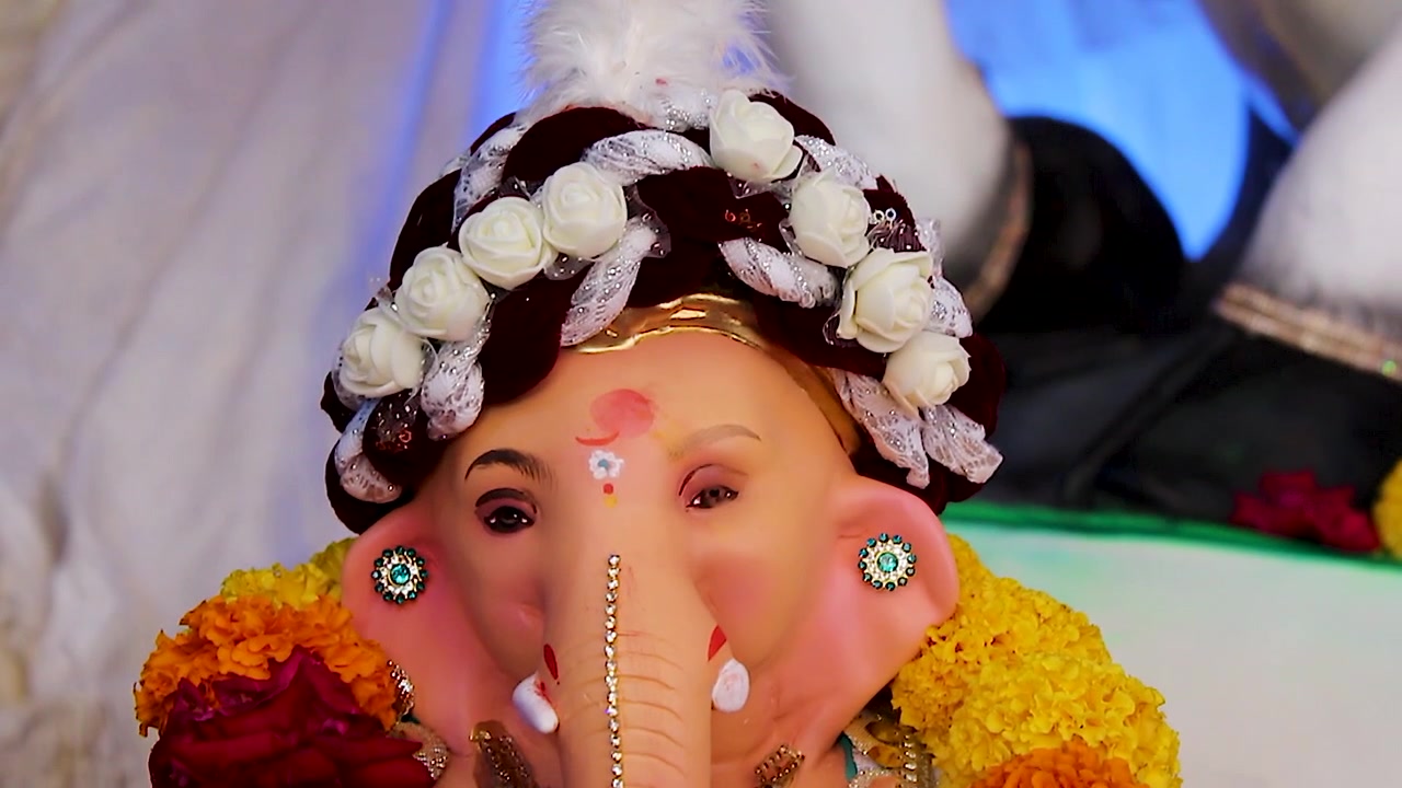 Primo piano del volto dell'idolo di Mangalmurti Ganesha che indossa un turbante di rose bianche e una ghirlanda di calendule, decorazione festiva del pandal per la celebrazione del Ganesh Chaturthi in India