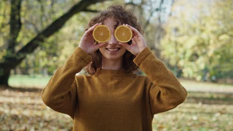 caucasian woman holding oranges in hands and covering eyes at the autumn park.