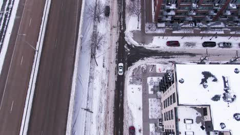 white car driving down snowy roads in a downtown city past a highway and buildings