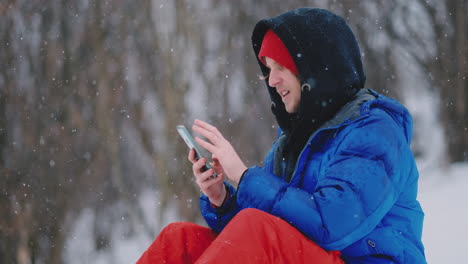 a male snowboarder sitting on the snow takes photos on the phone of a beautiful resort landscape for social networks. resort blogger