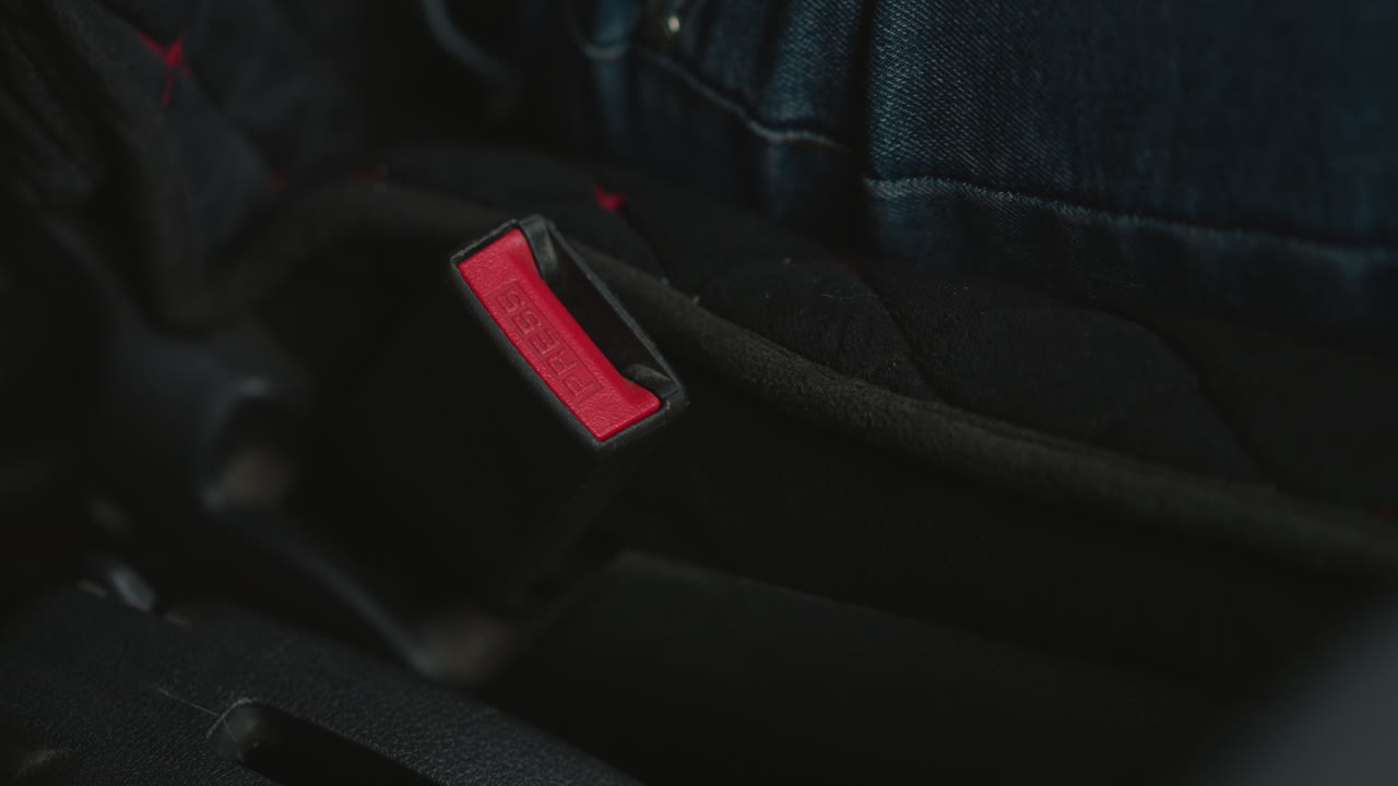 Close up of young adult hand locking seat belt buckle in car cabin focusing on finger pressing red latch under ambient lighting highlighting safety gesture and buckle mechanism detail