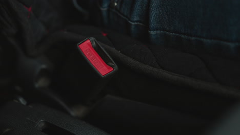 close up of young adult hand locking seat belt buckle in car cabin focusing on finger pressing red latch under ambient lighting highlighting safety gesture and buckle mechanism detail
