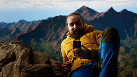 viajero con ropa cálida desplazándose por las redes sociales en la cima de la montaña