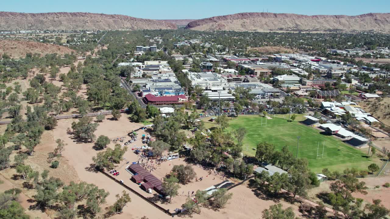 Aerial view of Alice Springs, Mparntwe and then panning down to the Henly on Todd Regatta on the dry river bed of the Todd River. Northern Territory, Australia. August 2022.