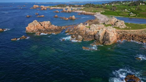 Tilted drone movement along the scattered rocky formations of Site du Gouffre on a small green peninsula, Plougrescant, Côtes-d'Armor, Brittany, France
