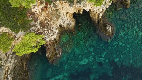 Insel-Kalamota,-Adria,-Kroatien---Das-Ruhige-Blaue-Wasser-Bildet-Einen-Kontrast-Zur-Zerklüfteten-Küstenlinie-Unter-Den-Vegetationsbedeckten-Klippen---Pullback-Aufstiegsaufnahme