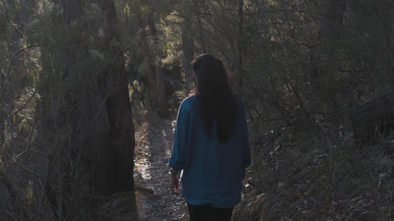 Una ragazza cammina attraverso la fitta foresta di Warrandyte a Melbourne. La scena cattura un momento sereno e contemplativo tra alberi alti e una luce soffusa e diffusa.