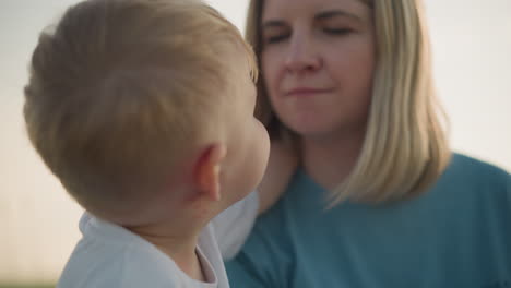 a joyful moment between a mother and her little boy in a grassy field. the boy, dressed in a white shirt, lovingly holds his mother's neck as she smiles at him, both sharing a happy connection