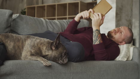hombre acostado en el sofá con su perro bulldog mientras lee un libro 1