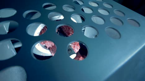 carne picada cayendo de una máquina de picado en una vista de arriba a través de una placa de metal con agujeros