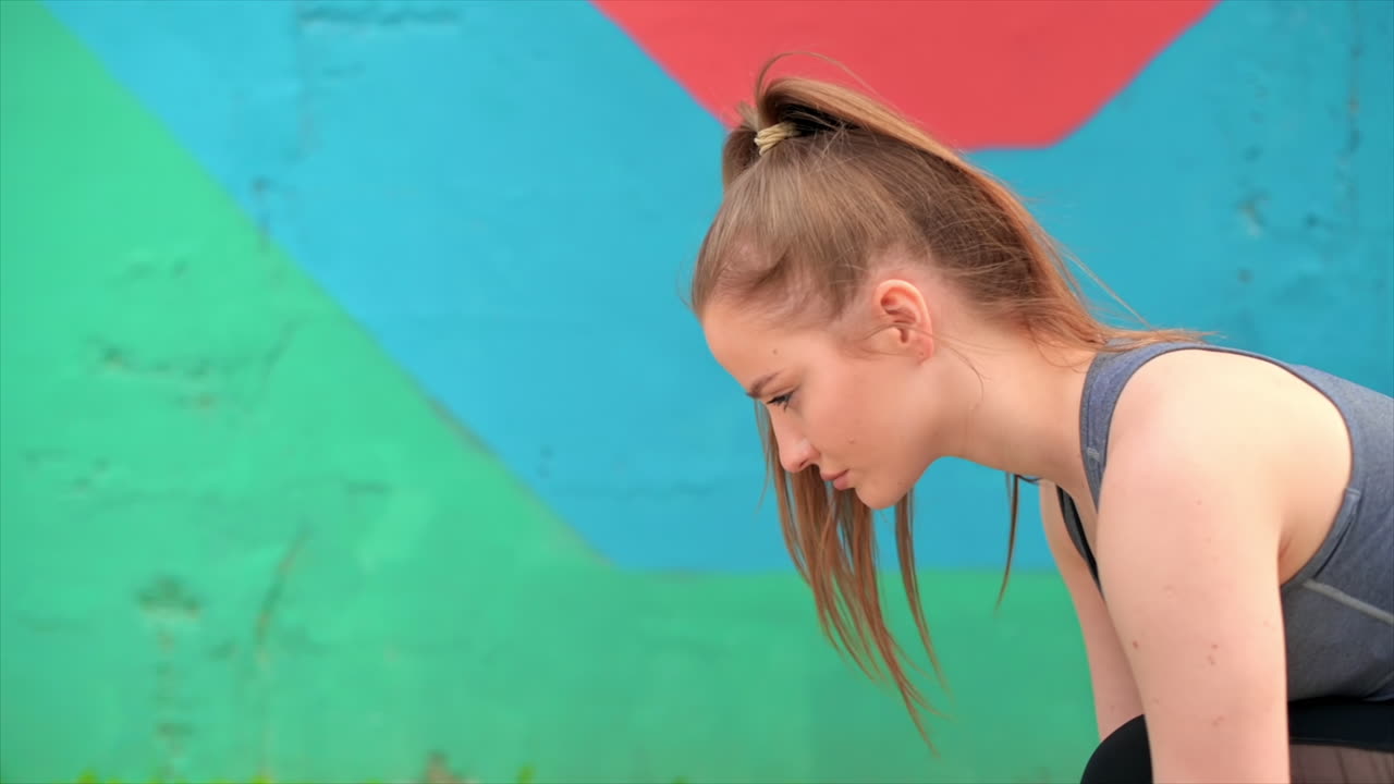 Young focused blonde woman at outdoors training preparing to starting running, multicolored background. Slow motion