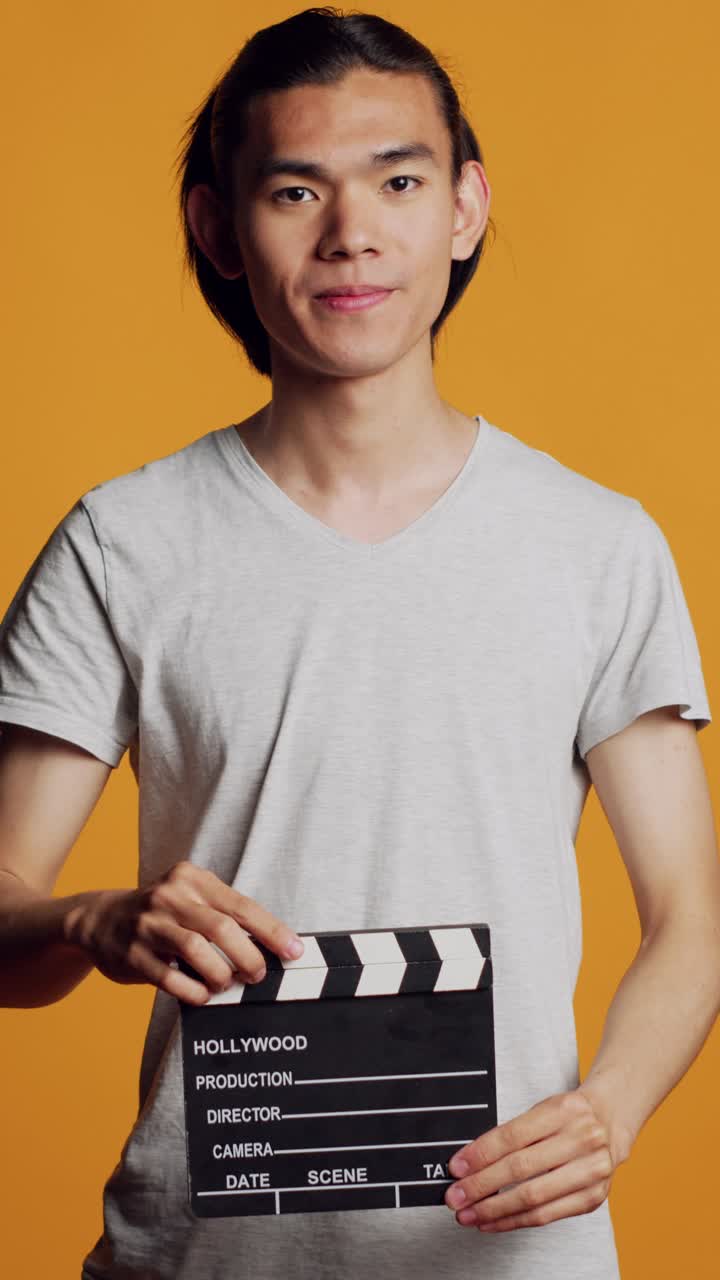 Vertical video: Casual modern man using film slate in studio