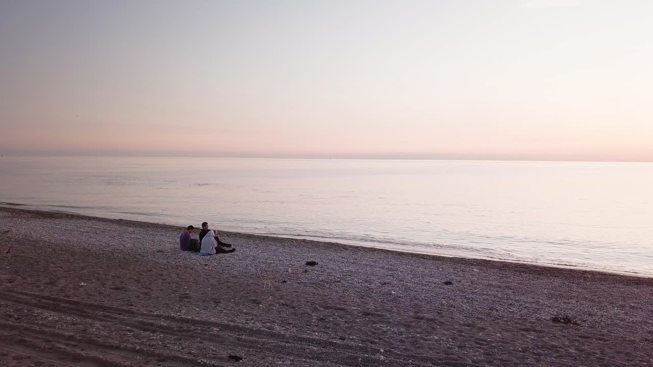 three friends sitting on the beach watching the sunset