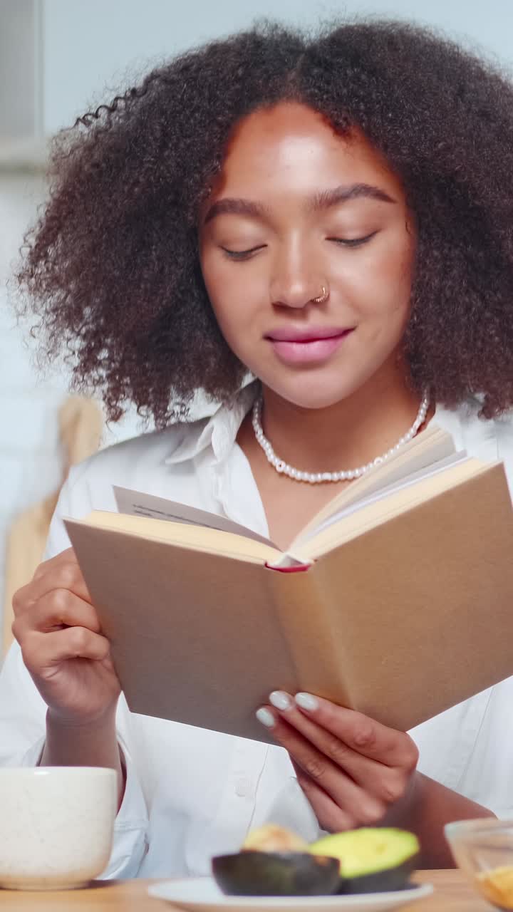 Junge schöne Afroamerikanerin frühstückt und liest ein Buch.