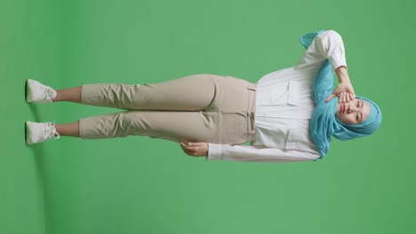 full body of asian muslim woman showing thumbs down gesture to camera while standing in the green screen background studio