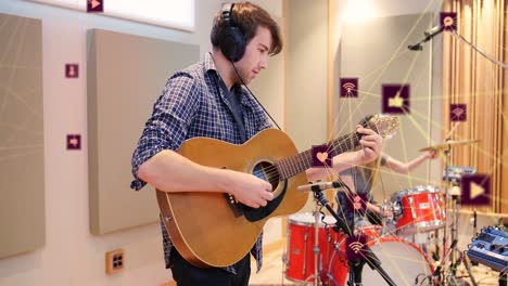 Animation-Verbundener-Symbole,-Die-Einen-Globus-über-Einem-Kaukasischen-Mann-Bilden,-Der-Bei-Proben-Im-Studio-Gitarre-Spielt