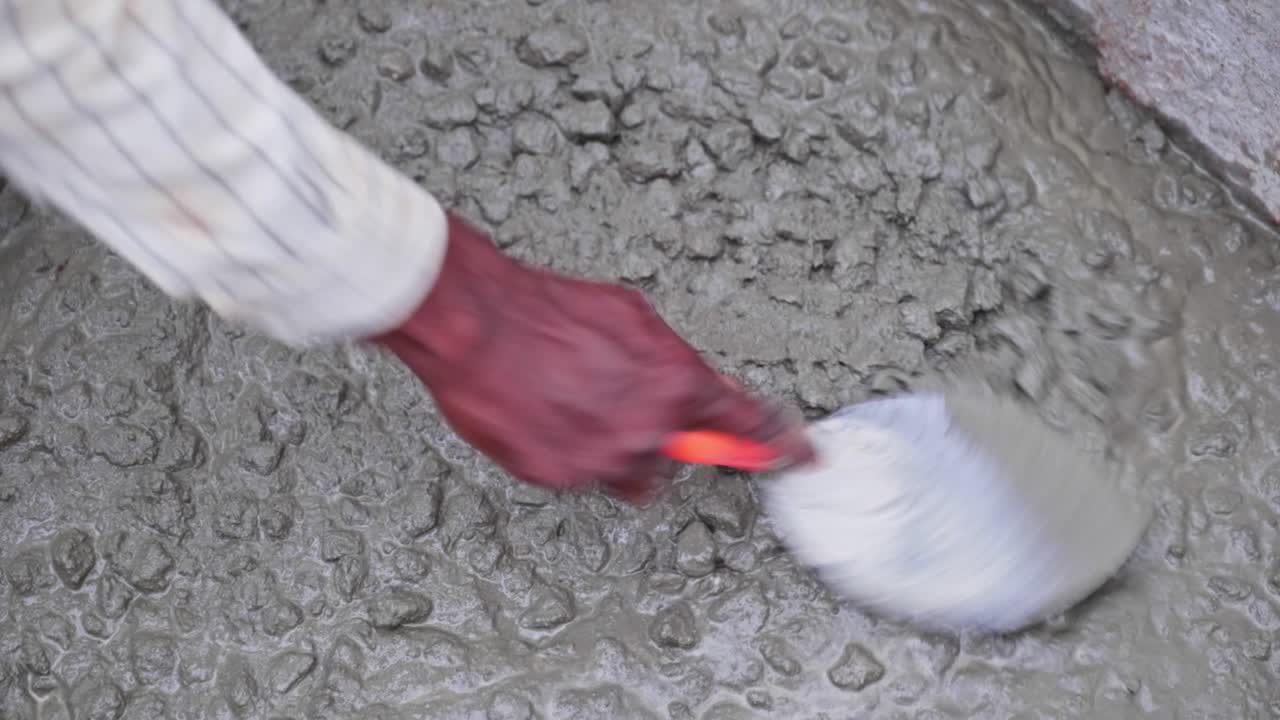 Primo piano di un operaio edile che usa una cazzuola per la finitura di cemento appena versato in cantiere. Di giorno, ripresa stabile, 4k
