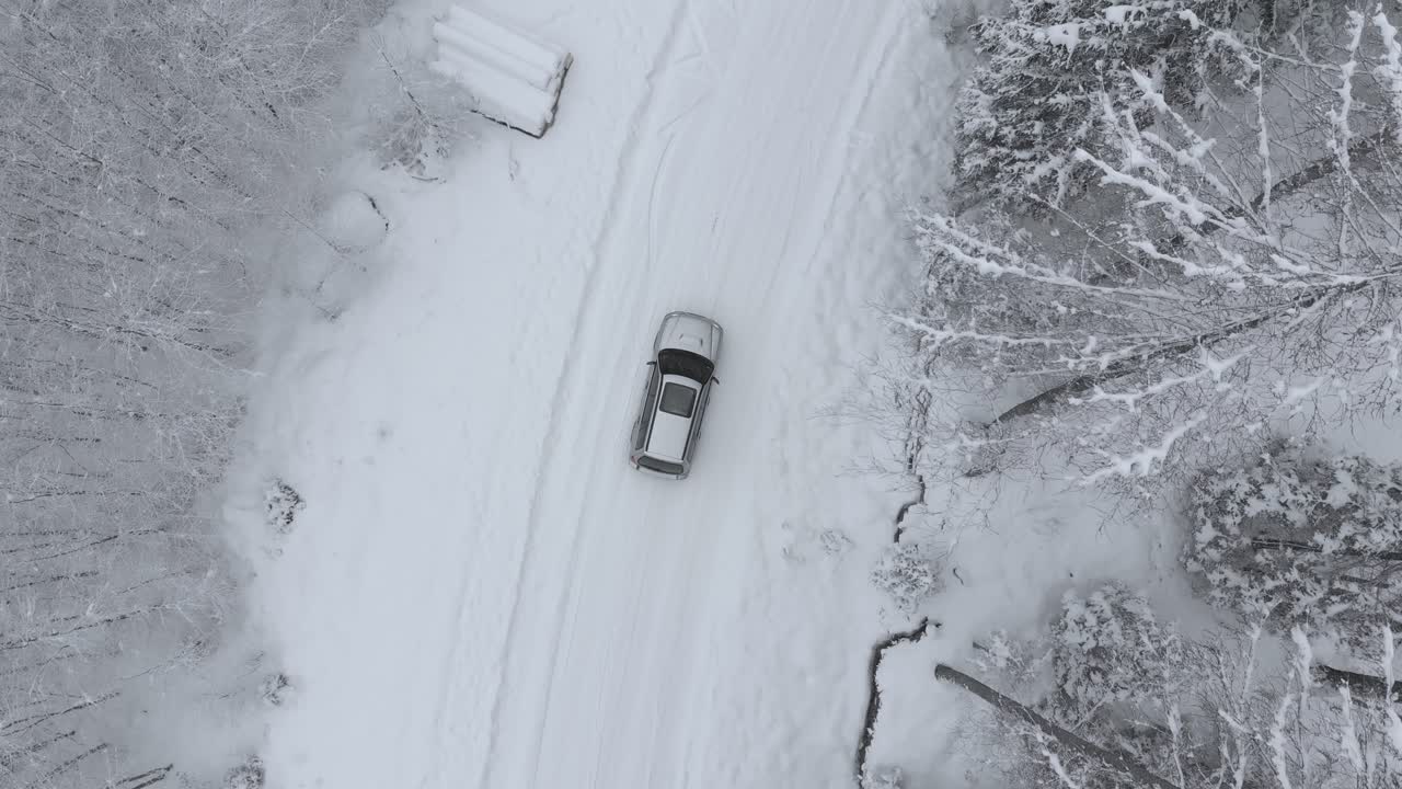 vista aérea de un camión en la carretera nevada girando a la derecha en medio de árboles cubiertos de nieve en un bosque congelado, en un día de invierno - disparo de drones, disparo de seguimiento, de arriba hacia abajo