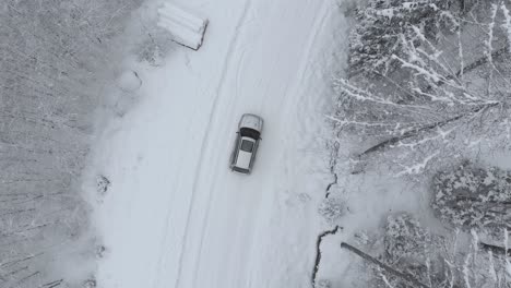 aerial view shot of a car on the snowy road turning right in middle of snow covered trees in frozen forest, on a winter day - drone shot, tracking shot, top down